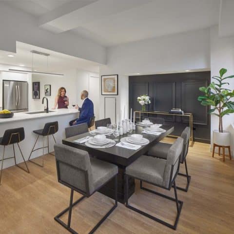 The kitchen and dining room at 101 dupont place. The dining room table is set out with white dishes and placemats and candles. The kitchen features a breakfast bar with marble counters and white cabinets, and stainless steel appliances.